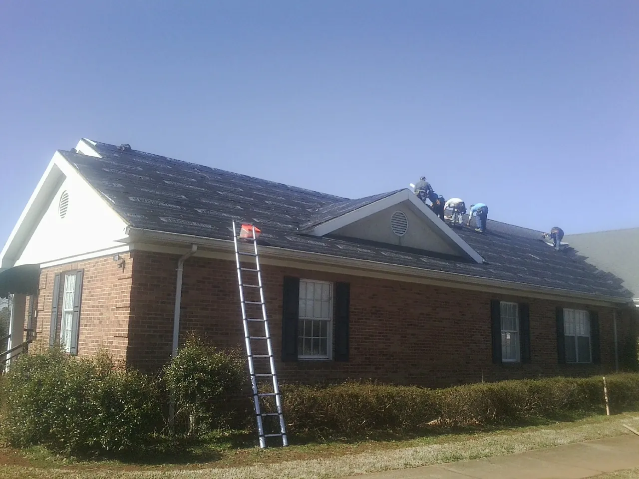 Crew tearing shingles off a brick ranch roof with a ladder set — Emergency Roof Repair work by our crew in Eagle Point