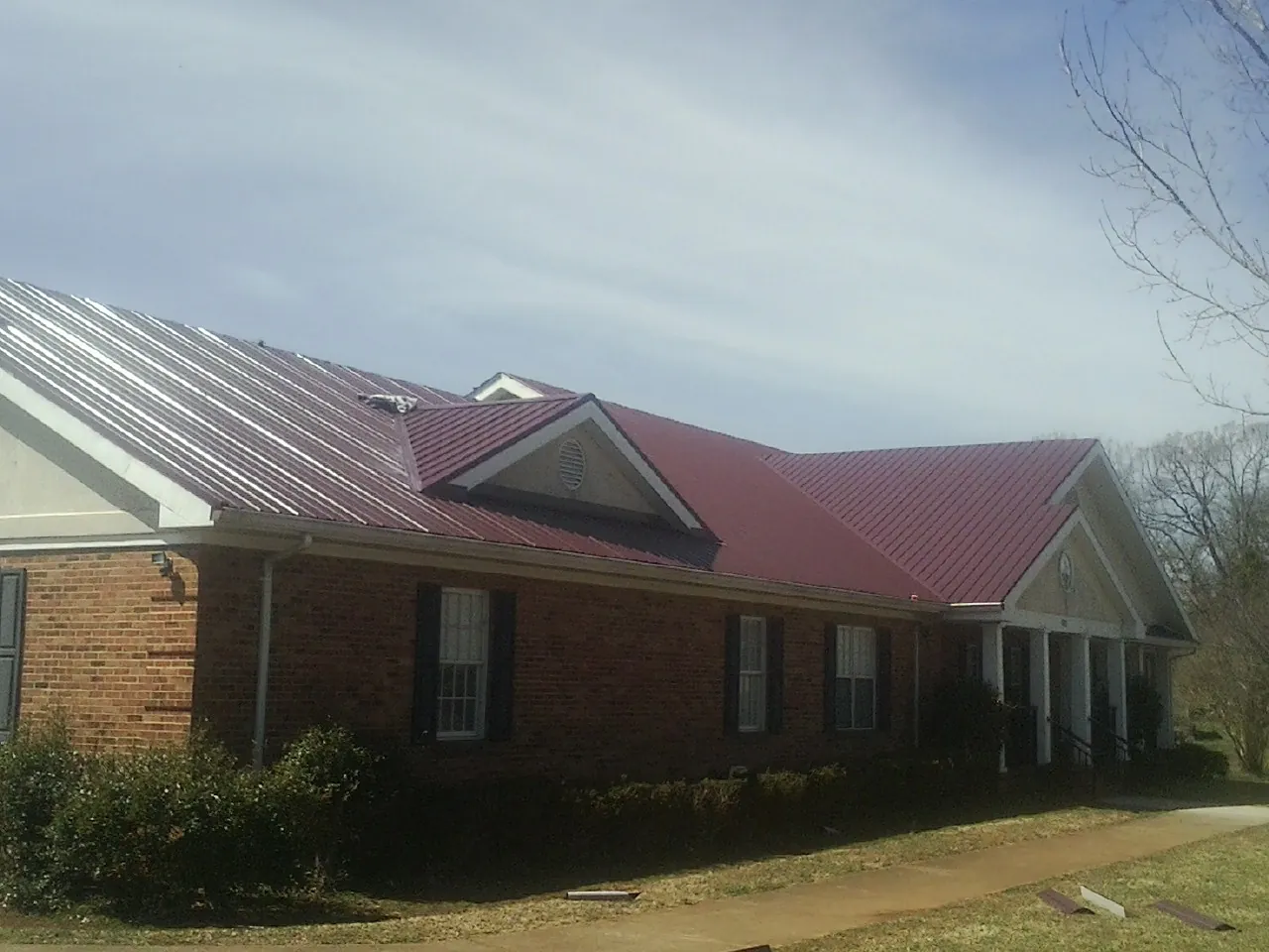 Red metal roof with gabled entries on a long brick building, from a Hail Damage Roof Repair job in Eagle Point