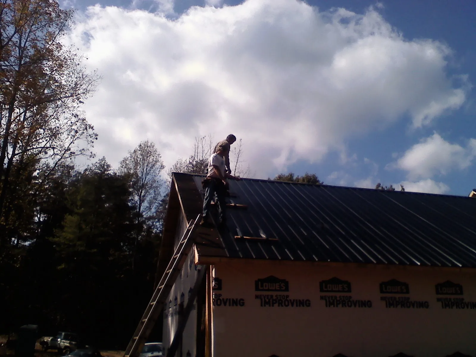 Roofer fastening dark metal panels high against a cloudy sky, from a Roof Inspection job in Eagle Point